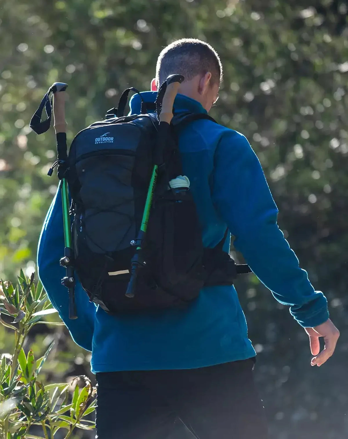 תרמיל טיולים אורטופדי Outdoor Revolution Camp 30L על גב מטייל עם מקלות הליכה, שרוכים אלסטיים לאבטוח
