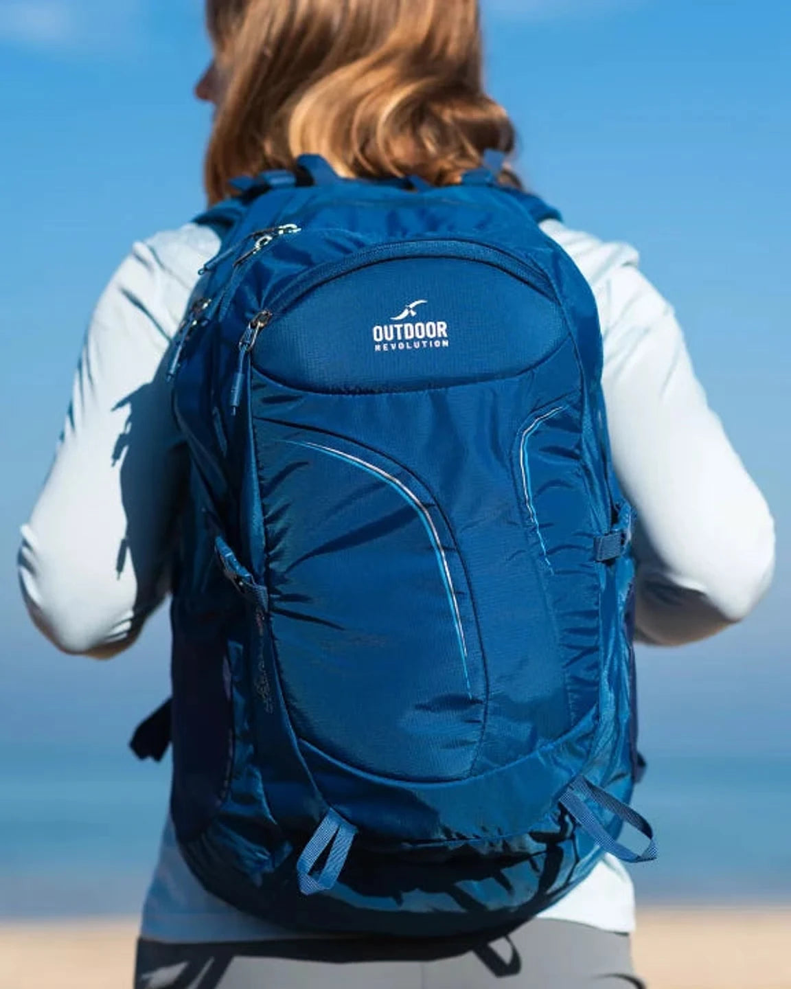 תרמיל יום Outdoor Revolution Makalu 28 ליטר בצבע כחול נייבי על גב מטיילת מול ים פתוח