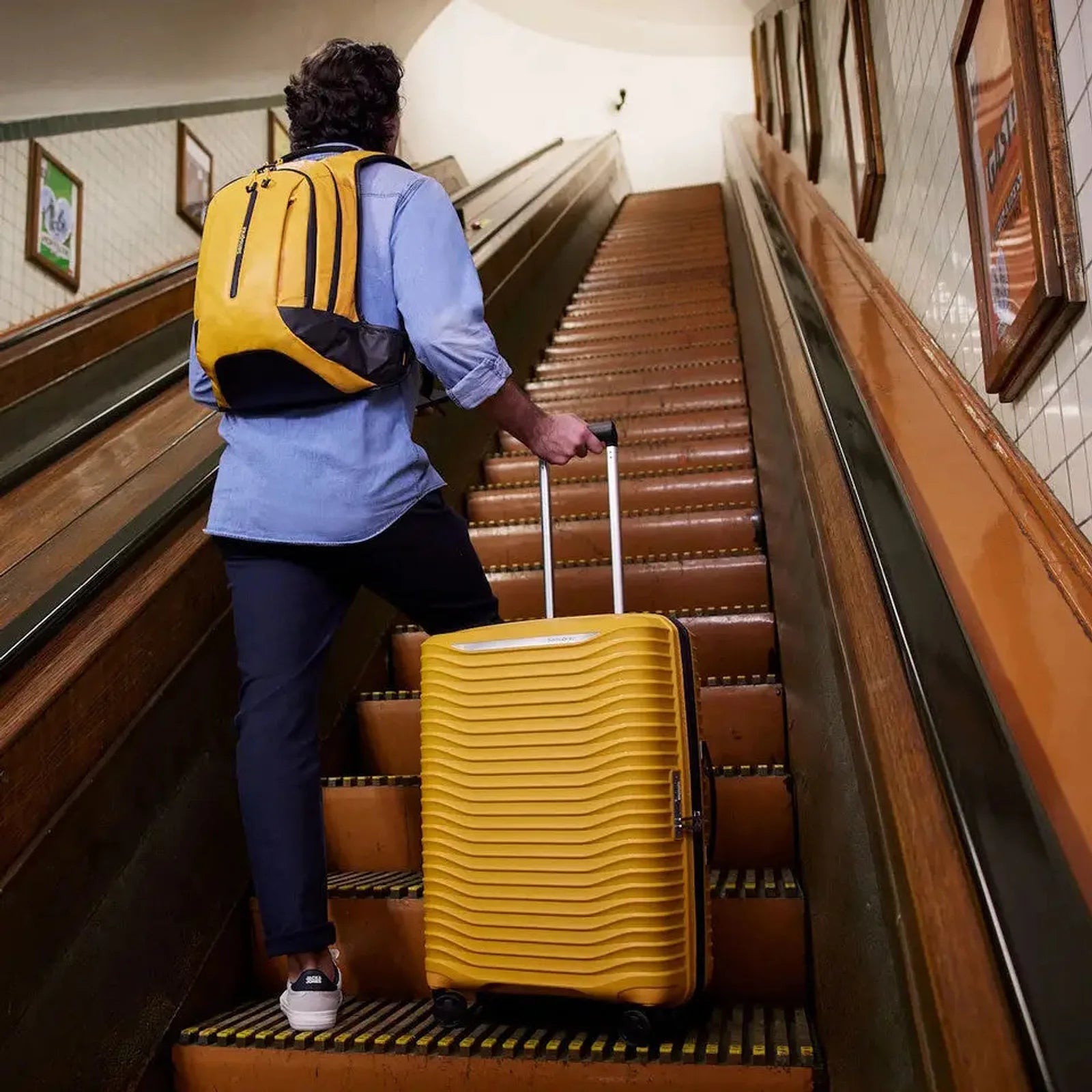 נוסע עולה במדרגות עם מזוודה קשיחה Samsonite Upscape בצבע צהוב - גלגלי סיליקון עם בולמי זעזועים