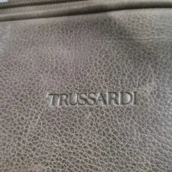 תקריב לוגו TRUSSARDI חרוט על עור ברידג' איטלקי איכותי, מראה מרקם העור האמיתי והתפר המוקפד של התיק
