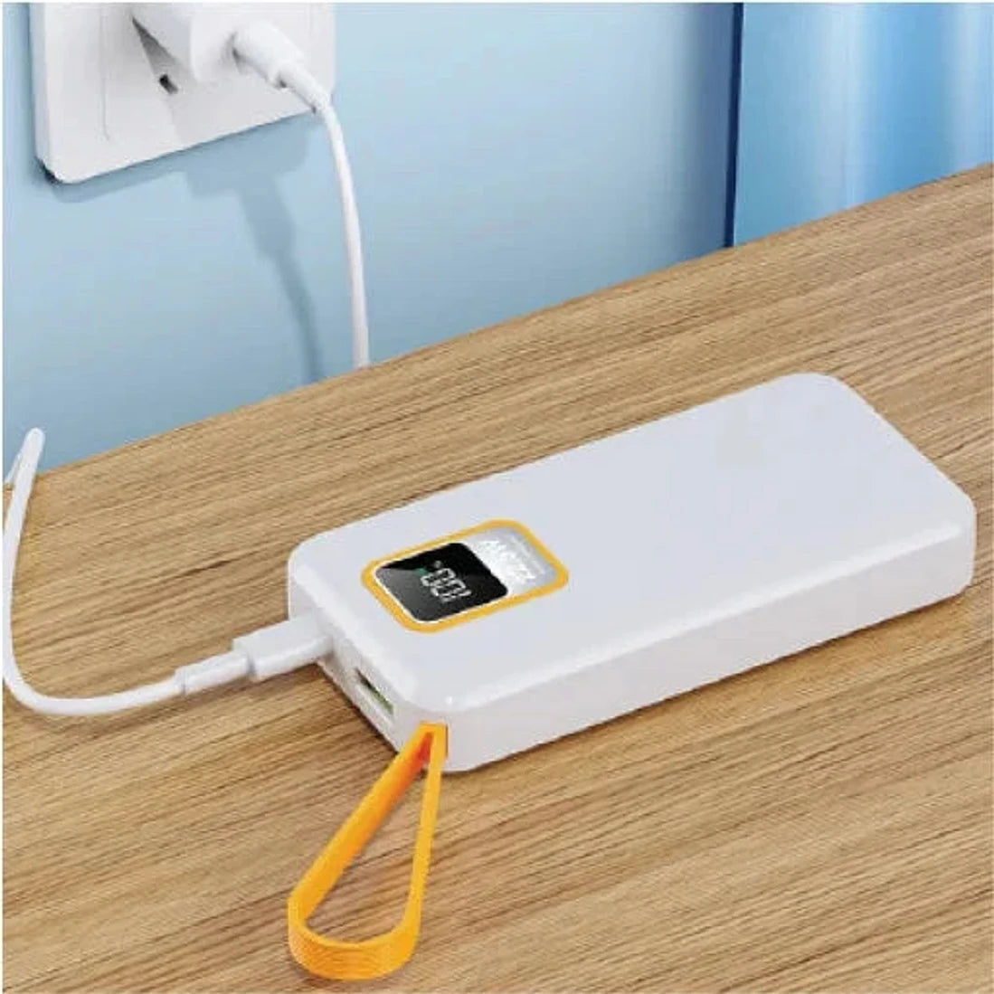 מטען נייד Charge-It 10000mAh לבן מחובר לשקע לטעינה, מוצב על שולחן עם כבל USB, נוח לנסיעות