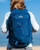 תרמיל יום Outdoor Revolution Makalu 28 ליטר בצבע כחול נייבי על גב מטיילת מול ים פתוח