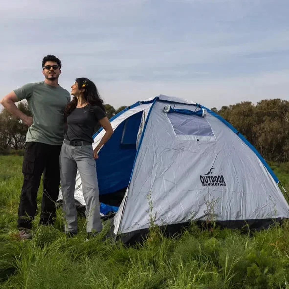 זוג מטיילים ליד אוהל איגלו Outdoor Revolution Revolution 2PR בשדה ירוק, הרכבה מהירה של 2 דקות