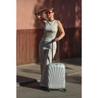 מזוודת טרולי Samsonite C-lite 20 אינץ׳ אוף-ווייט במשקל 1.9 ק״ג לצד דוגמנית ברחוב, לעליה למטוס