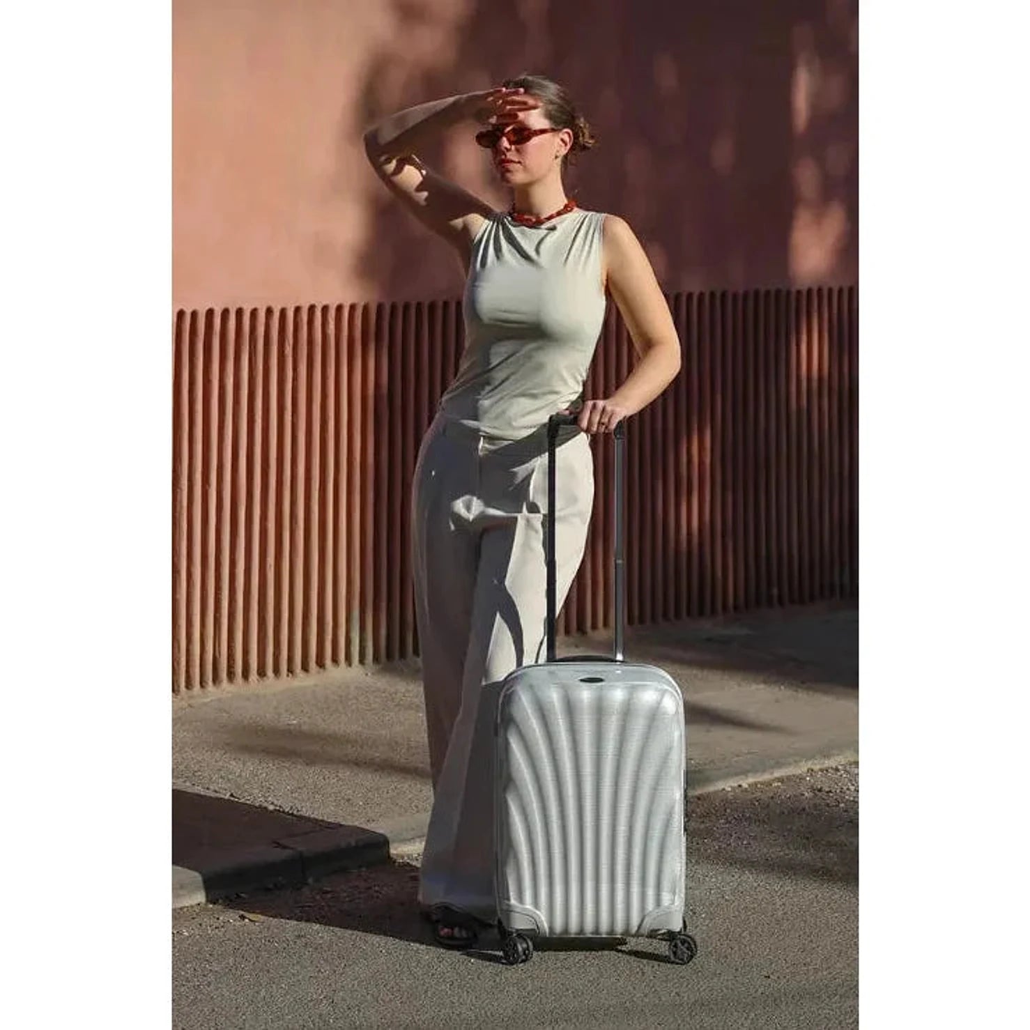 מזוודת טרולי Samsonite C-lite 20 אינץ׳ אוף-ווייט במשקל 1.9 ק״ג לצד דוגמנית ברחוב, לעליה למטוס